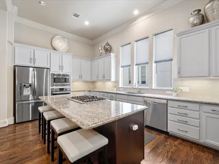 a kitchen with stainless steel appliances granite countertop a stove top oven a refrigerator a dining table and chairs with wooden floor