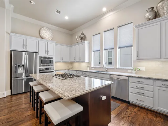 a kitchen with stainless steel appliances granite countertop a stove top oven a refrigerator a dining table and chairs with wooden floor