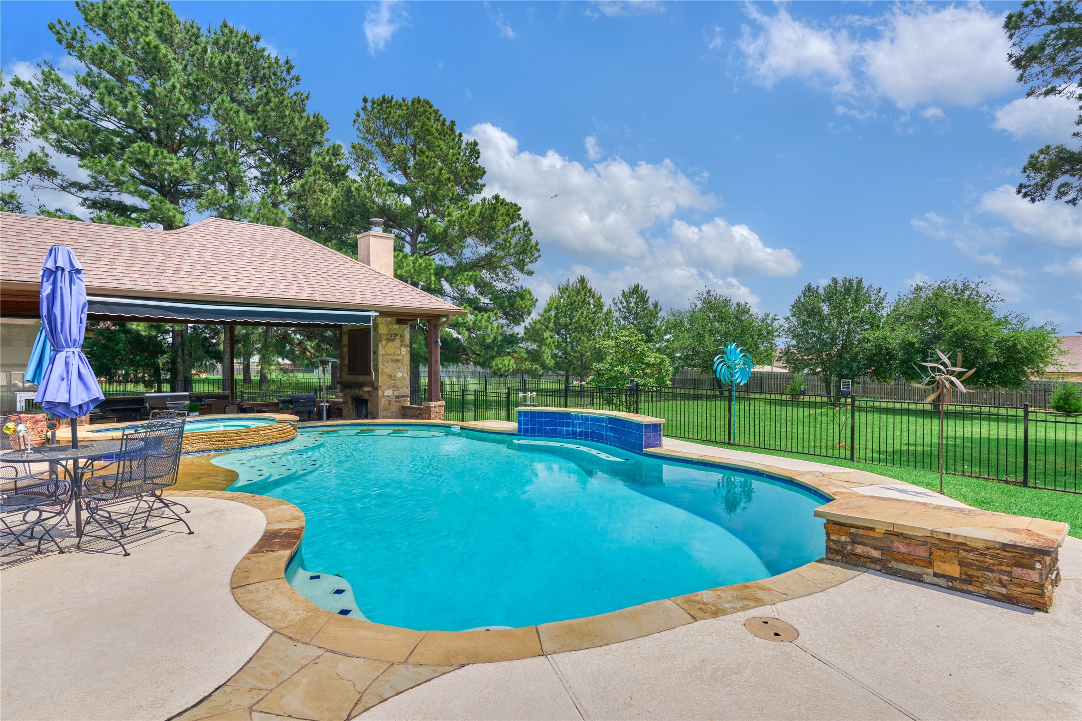 19089 Grandview Point Montgomery, TX 77356 - Photo 5 of 48 This backyard features a spacious pool with a stone deck, surrounded by lush greenery and mature trees. There's a covered patio with outdoor seating and a fireplace, perfect for entertaining.