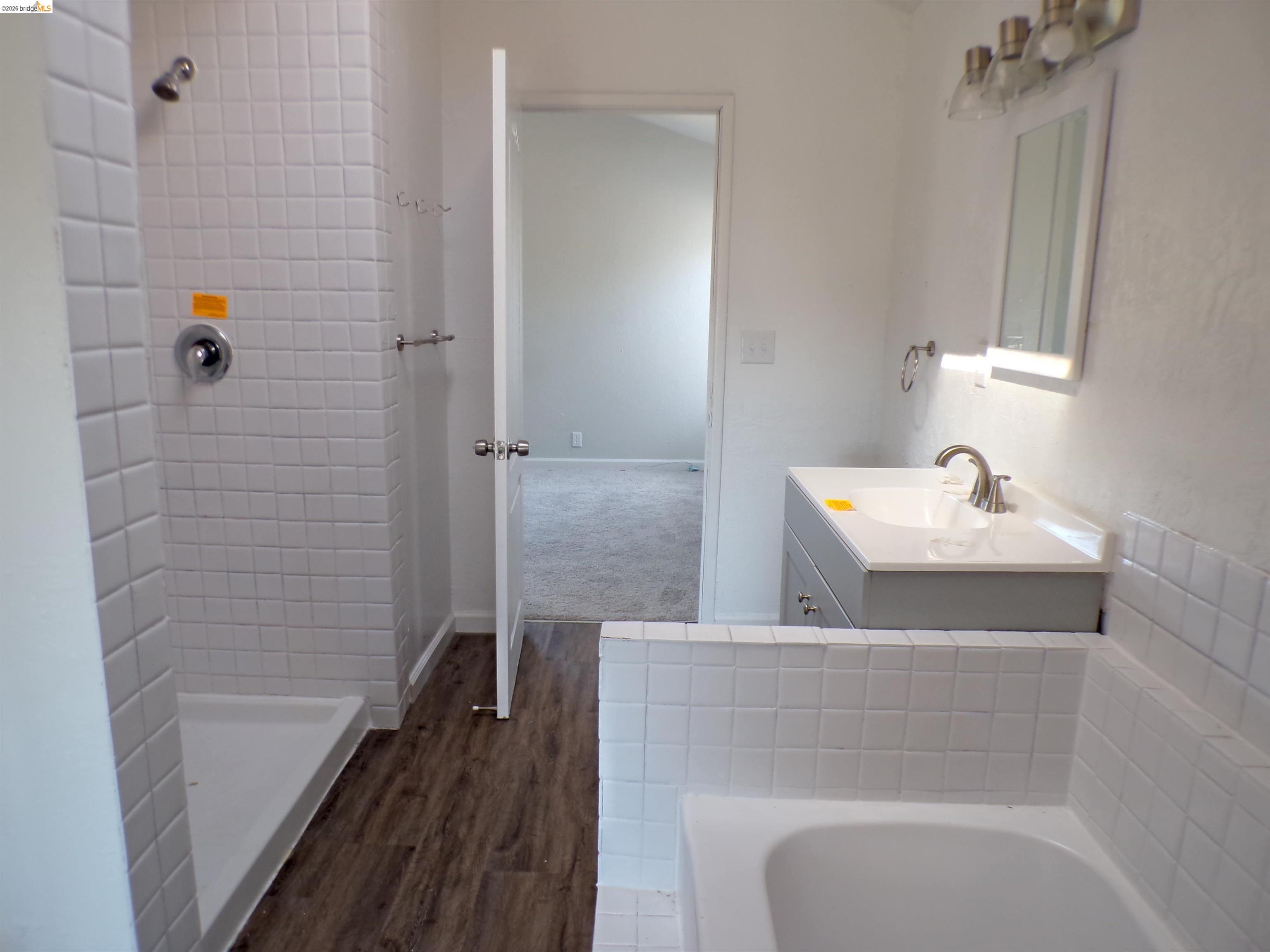 4271 Council Trail Copperopolis, CA 95228 - Photo 24 of 32 Bathroom featuring a white tile shower, integrated bathtub, a gray vanity with a white countertop and basin sink, and wood-finish flooring