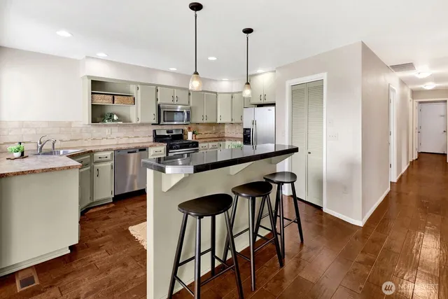 a kitchen with stainless steel appliances granite countertop a stove a sink a refrigerator and a wooden floor