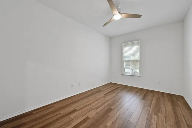 an empty room with wooden floor chandelier fan and windows