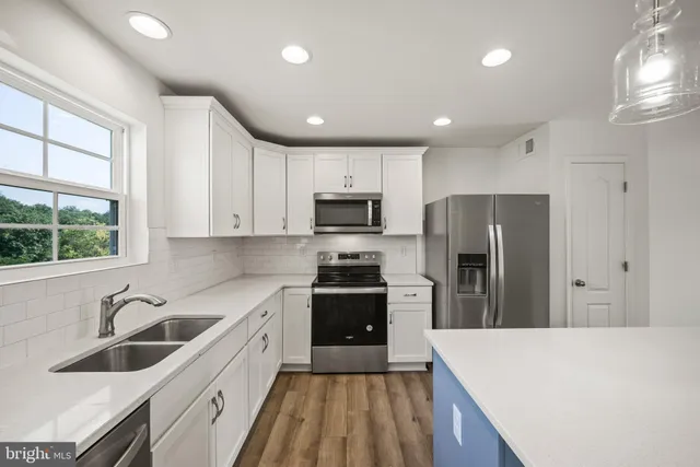 a large kitchen with stainless steel appliances granite countertop a sink dishwasher a refrigerator and a stove with wooden floor