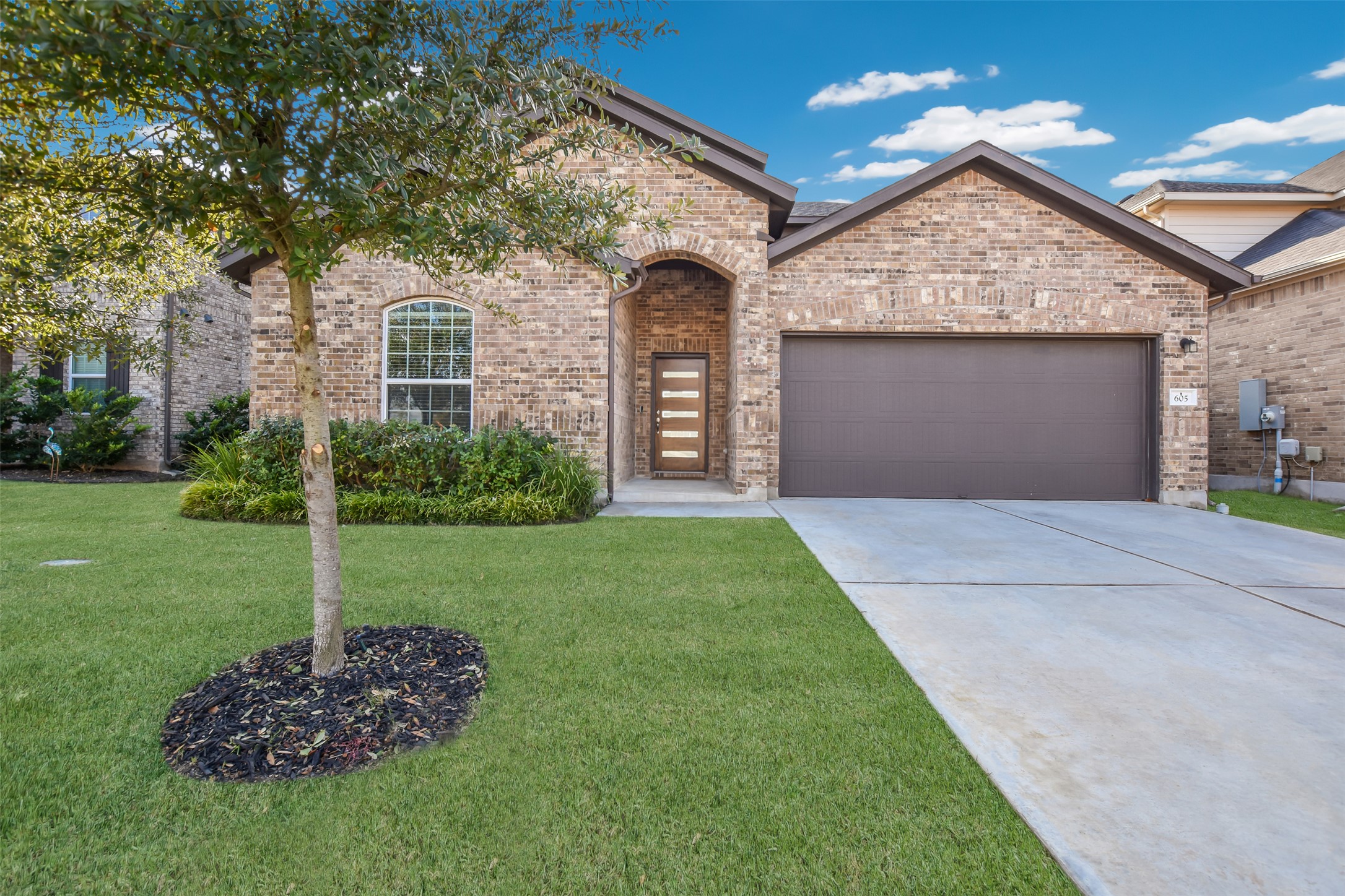 French provincial home with driveway, brick siding, a front yard, and an attached garage