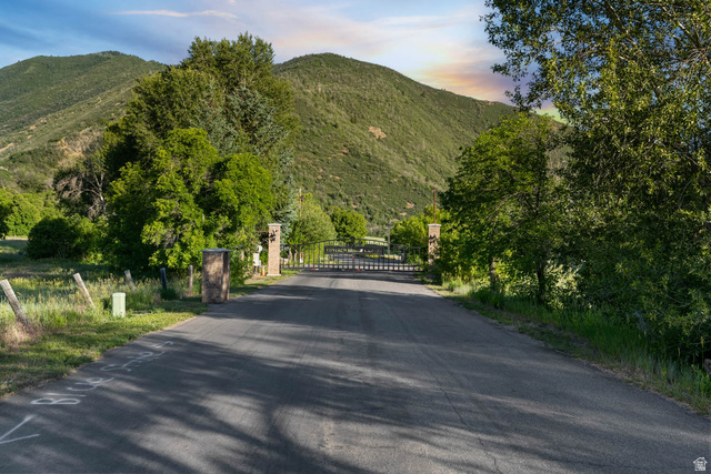 10686 South Covered Brg Cyn Road, Unit 14 Spanish Fork, UT 84660 - Photo 3 of 44 Paved driveway leading to a gated entry, flanked by stone pillars and mature trees, set against a backdrop of rolling, tree-covered hills