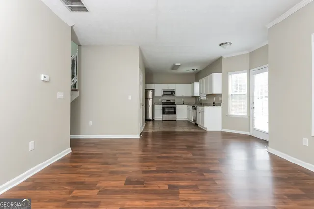 a view of empty room with wooden floor and kitchen view