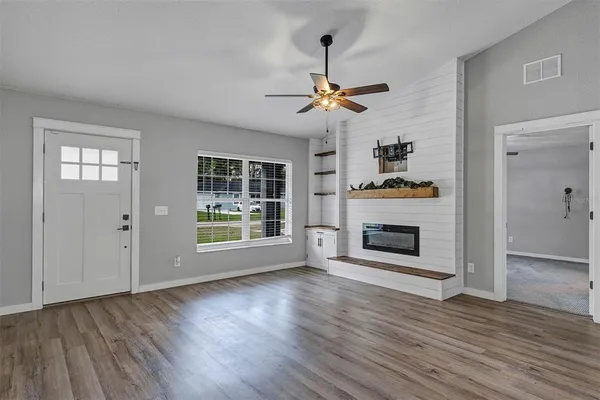 a view of a livingroom with a fireplace a ceiling fan and windows