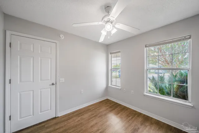 an empty room with wooden floor fan and windows