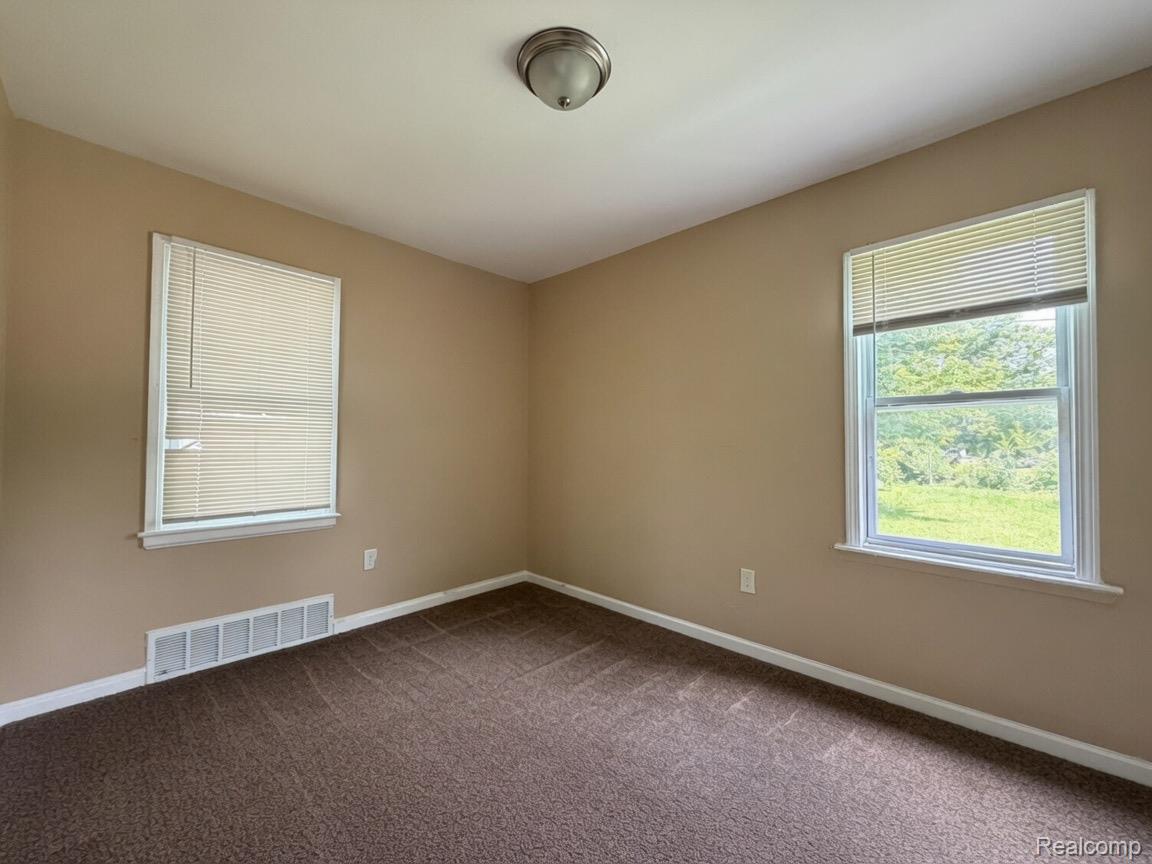 7286 Faust Avenue Detroit, MI 48228 - Photo 13 of 19 Spacious room featuring neutral tone walls, dark brown textured carpeting, two windows with white blinds, and a flush mount ceiling light fixture