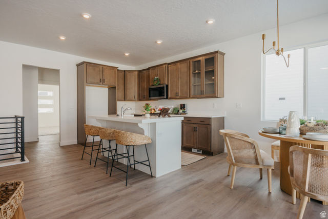 4595 North Fallow Way, Unit 511 Eagle Mountain, UT 84005 - Photo 13 of 32 Kitchen with a breakfast bar area, wood finish cabinetry, a kitchen island with sink, glass fronted cabinets, and light wood finished floors