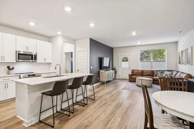a living room with stainless steel appliances a dining table wooden floor and a window