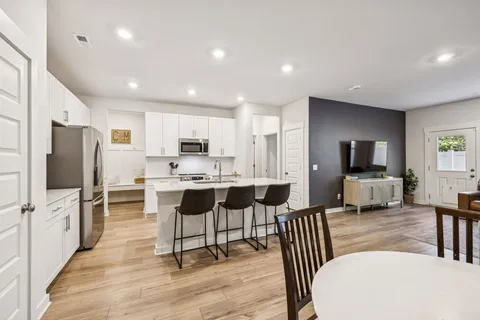 a living room with stainless steel appliances furniture a flat screen tv and kitchen view