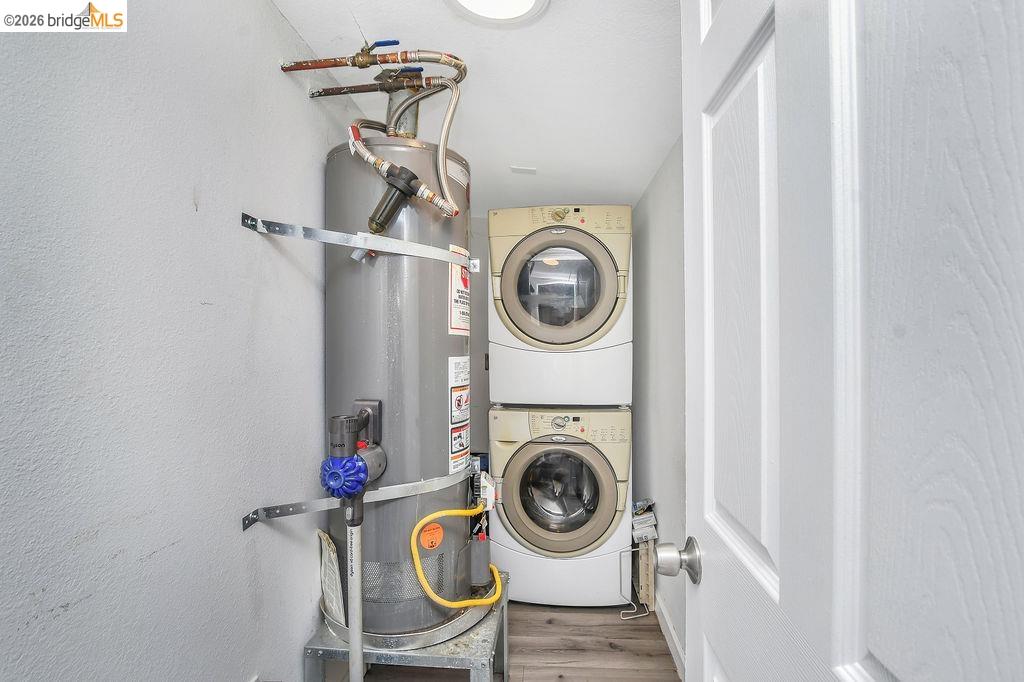 2191 East Cypress Road Oakley, CA 94561 - Photo 15 of 48 Laundry area featuring secured water heater, stacked washing machine and dryer, wood finished floors, and a textured wall