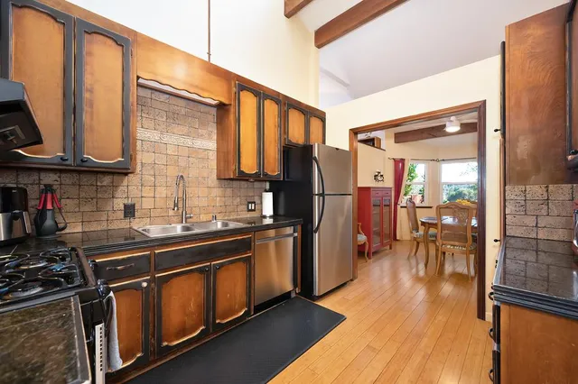 a kitchen with stainless steel appliances granite countertop a refrigerator a sink dishwasher a stove and a dining table with wooden floor