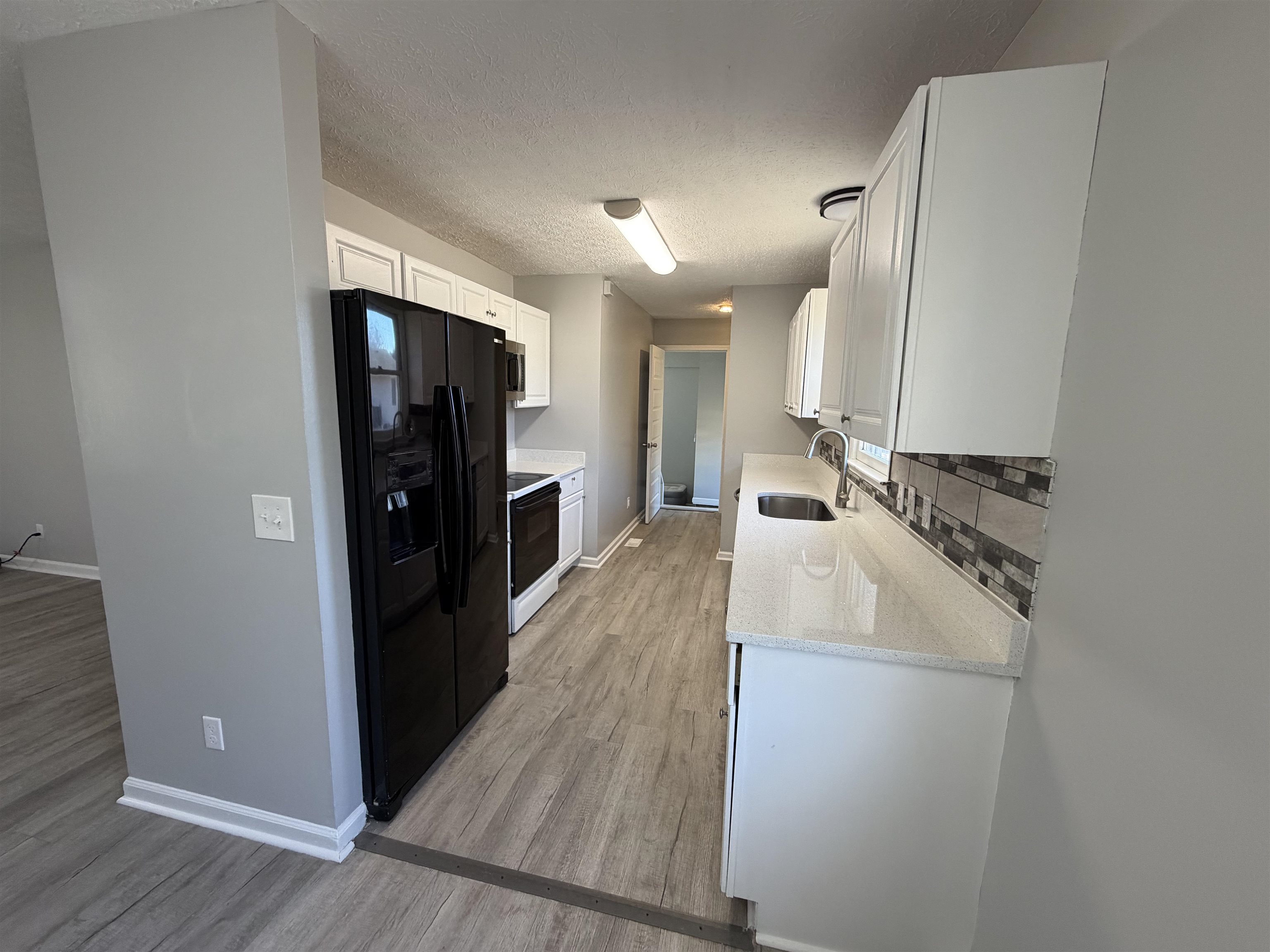 607 Geddings Drive Myrtle Beach, SC 29588 - Photo 6 of 21 Kitchen with light stone counters, white cabinetry, black fridge, a textured ceiling, and decorative backsplash