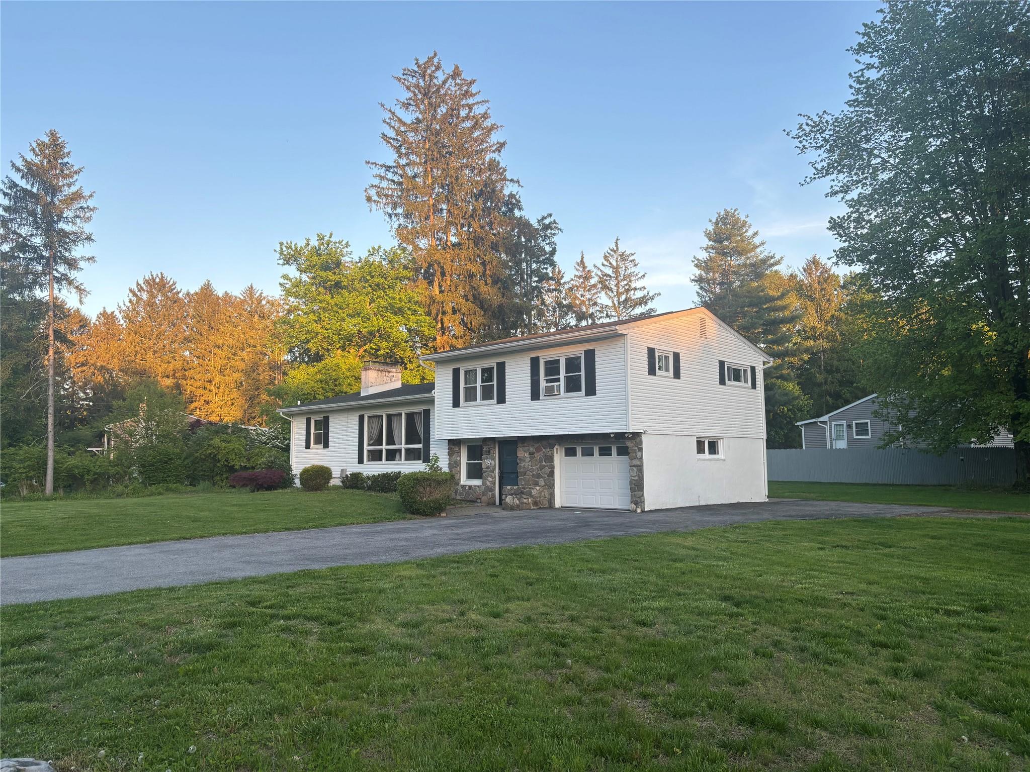 Tri-level home with asphalt driveway, a front lawn, a garage, a chimney, and stone siding