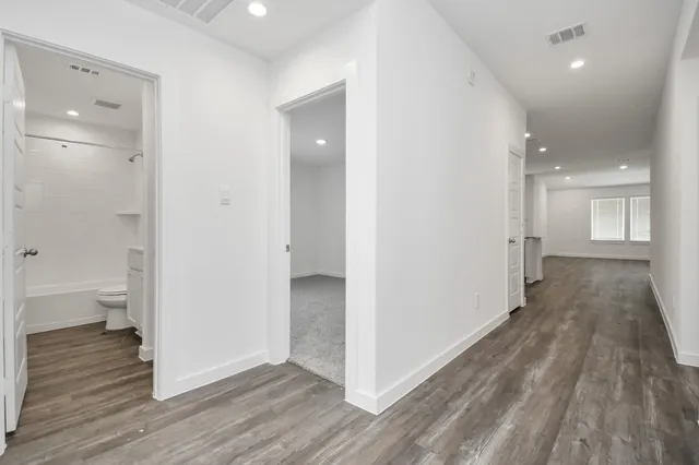 a view of a hallway with wooden floor and a bathroom