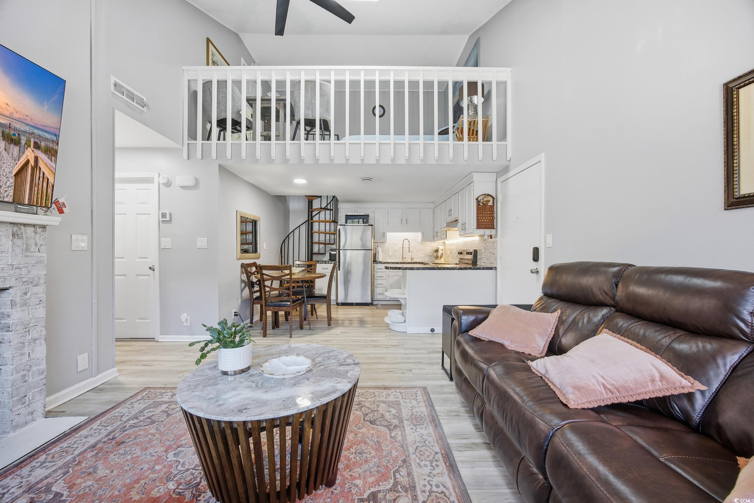 1200 Benna Drive, Unit 1C Myrtle Beach, SC 29577 - Photo 10 of 37 Living area with stairs, a towering ceiling, light wood-type flooring, a ceiling fan, and a fireplace with flush hearth