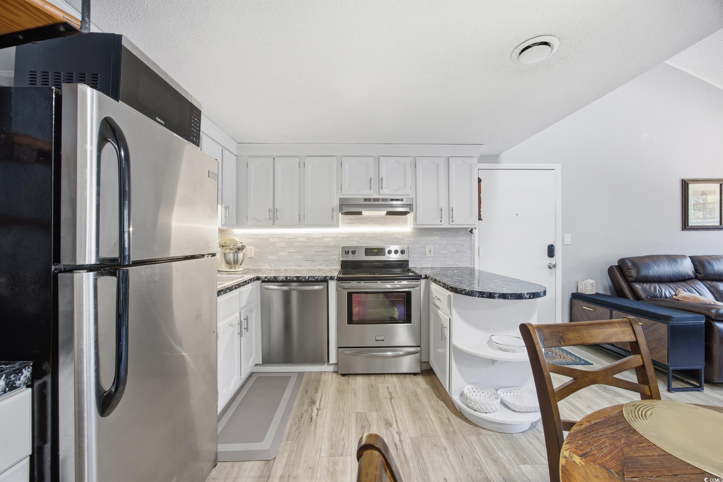 1200 Benna Drive, Unit 1C Myrtle Beach, SC 29577 - Photo 13 of 37 Kitchen featuring stainless steel appliances, tasteful backsplash, light wood-style flooring, dark stone counters, and white cabinetry