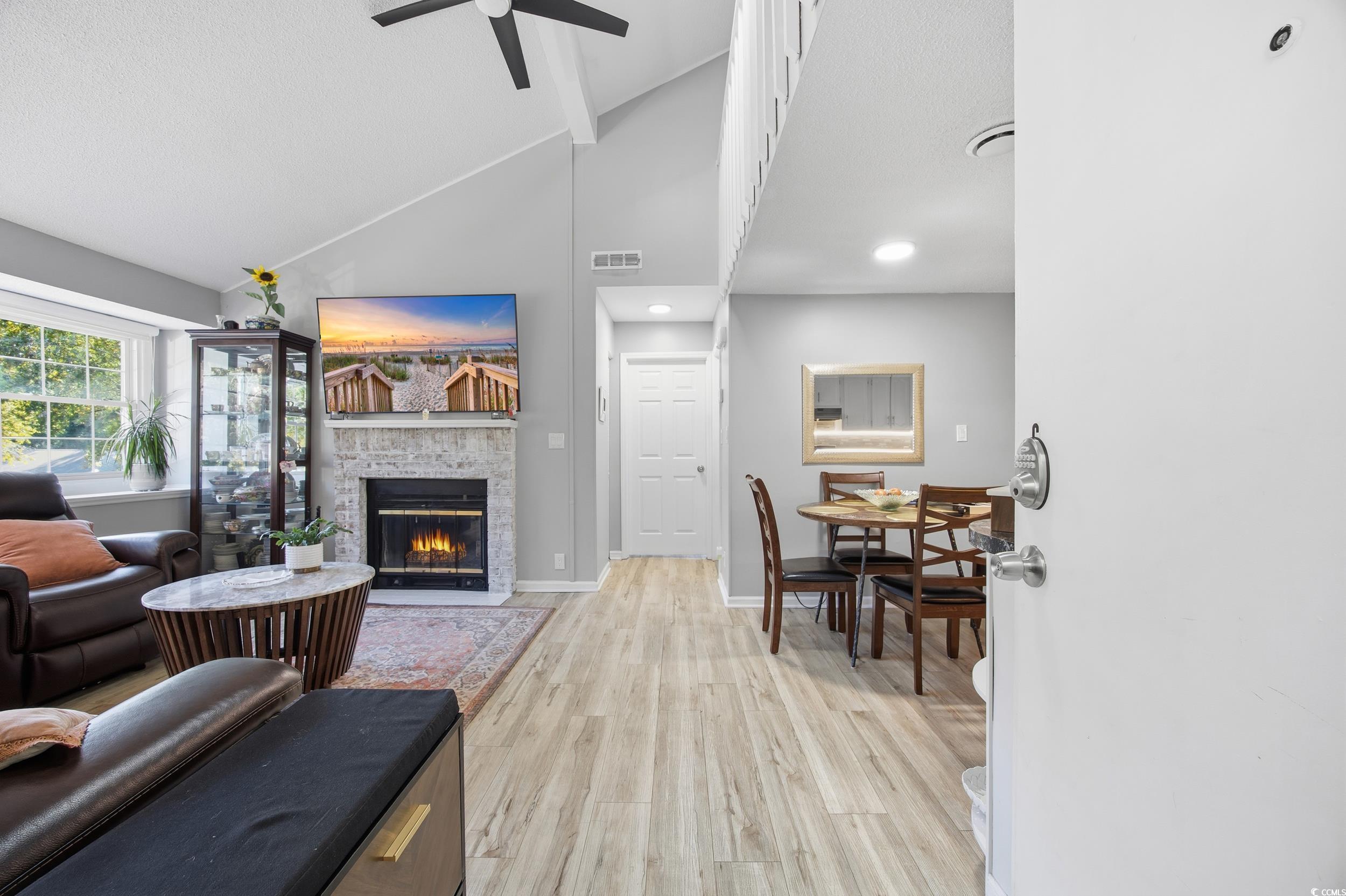 1200 Benna Drive, Unit 1C Myrtle Beach, SC 29577 - Photo 7 of 37 Living area with light wood-style flooring, a fireplace with flush hearth, high vaulted ceiling, and a ceiling fan