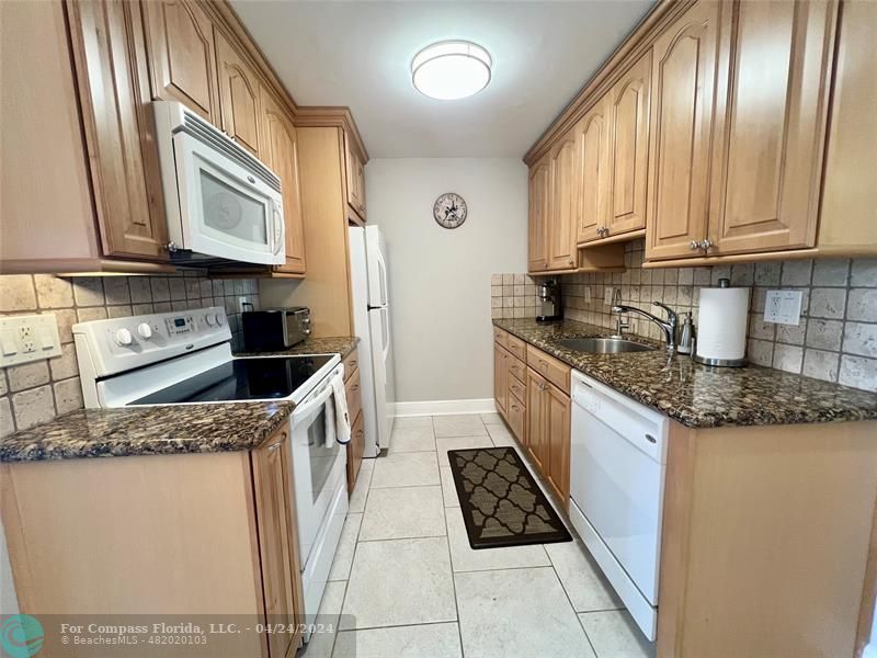 a kitchen with granite countertop a sink a stove top oven and cabinetry