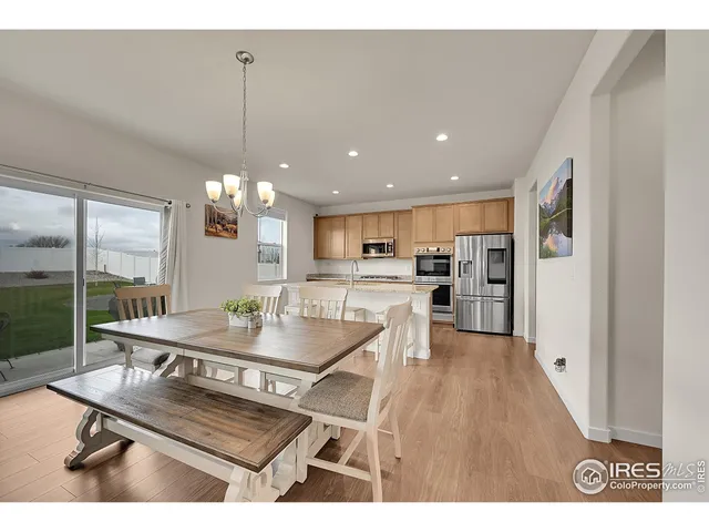 a room with stainless steel appliances kitchen island granite countertop a refrigerator a stove a kitchen island a dining table and chairs with wooden floor