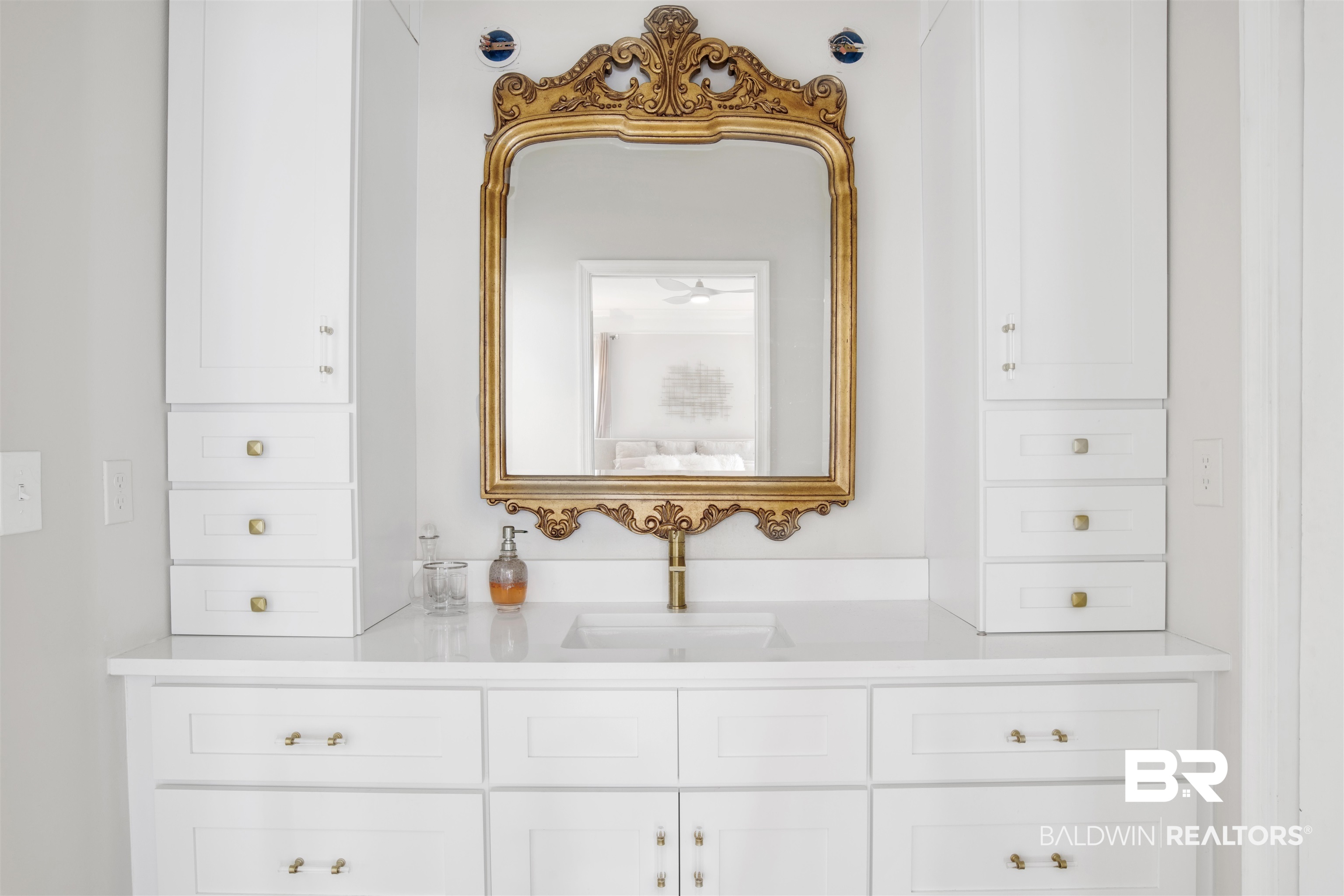 30351 River Road Orange Beach, AL 36561 - Photo 20 of 44 Double vanity featuring white cabinetry, a white countertop, an undermount sink, and brass-finish hardware