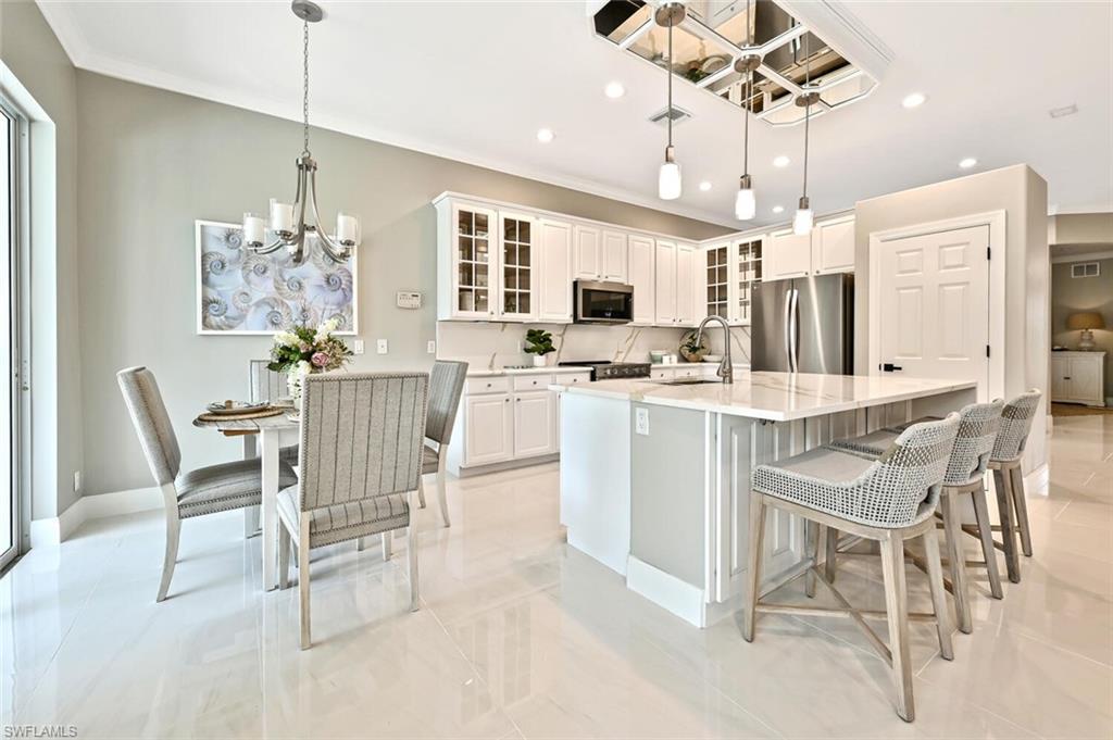 5616 Lago Villaggio Way Naples, FL 34104 - Photo 12 of 43 a dining room with stainless steel appliances kitchen island granite countertop a dining table chairs and a refrigerator