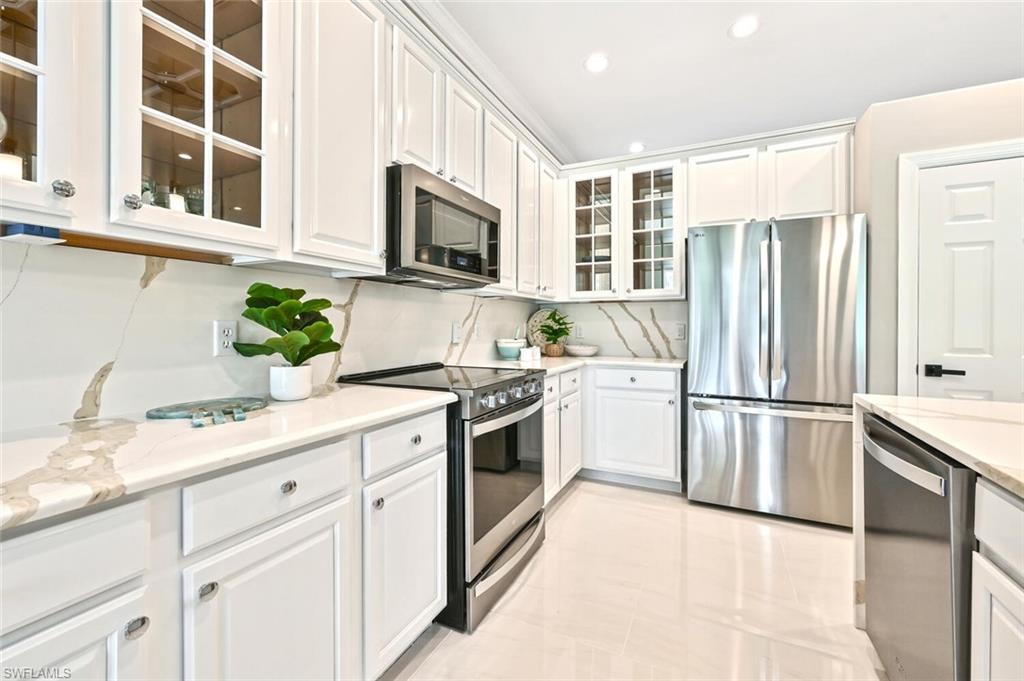 5616 Lago Villaggio Way Naples, FL 34104 - Photo 10 of 43 a kitchen with stainless steel appliances granite countertop white cabinets a microwave a sink and a refrigerator
