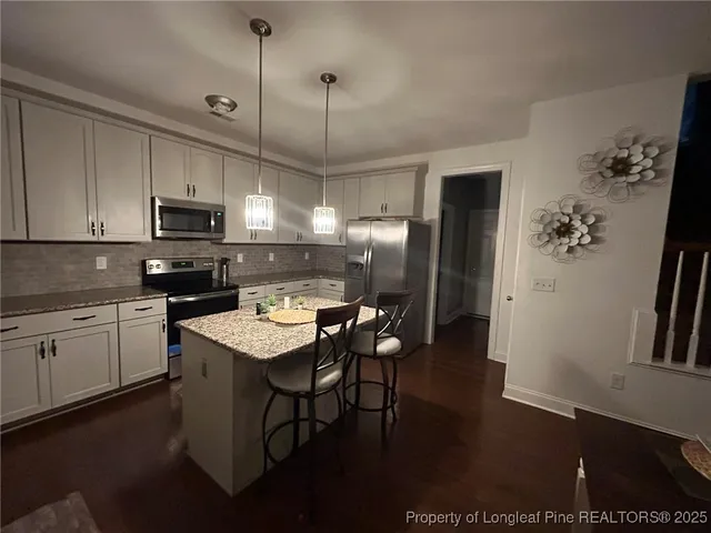 a kitchen with granite countertop a stove a refrigerator a sink a dining table and chairs