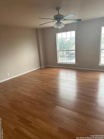 an empty room with wooden floor chandelier fan and windows