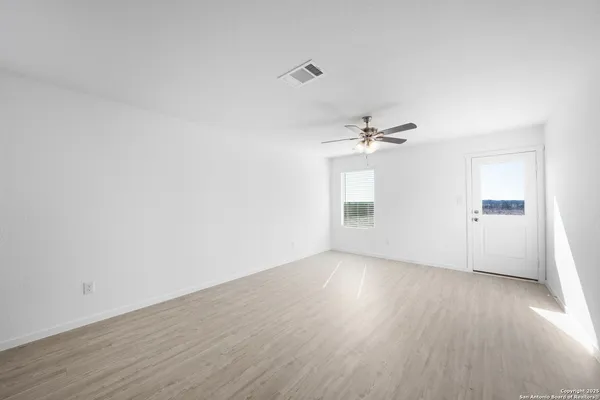 an empty room with wooden floor chandelier fan and windows