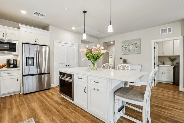 a kitchen with stainless steel appliances kitchen island granite countertop a refrigerator a stove a sink dishwasher and a dining table with wooden floor