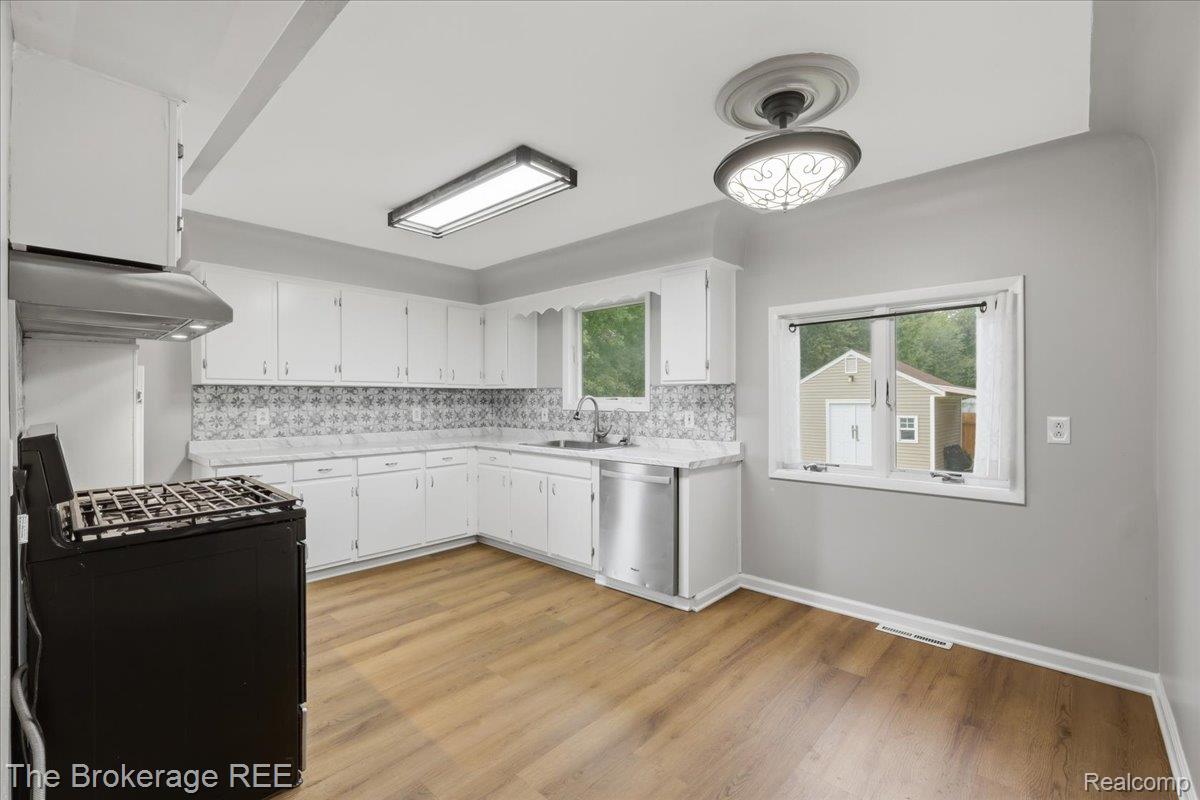 11973 East Brooks Road Lennon, MI 48449 - Photo 13 of 28 Kitchen featuring wood-finish flooring, white cabinetry, a patterned tile backsplash, stainless steel dishwasher, and a black range with a stainless steel vent hood