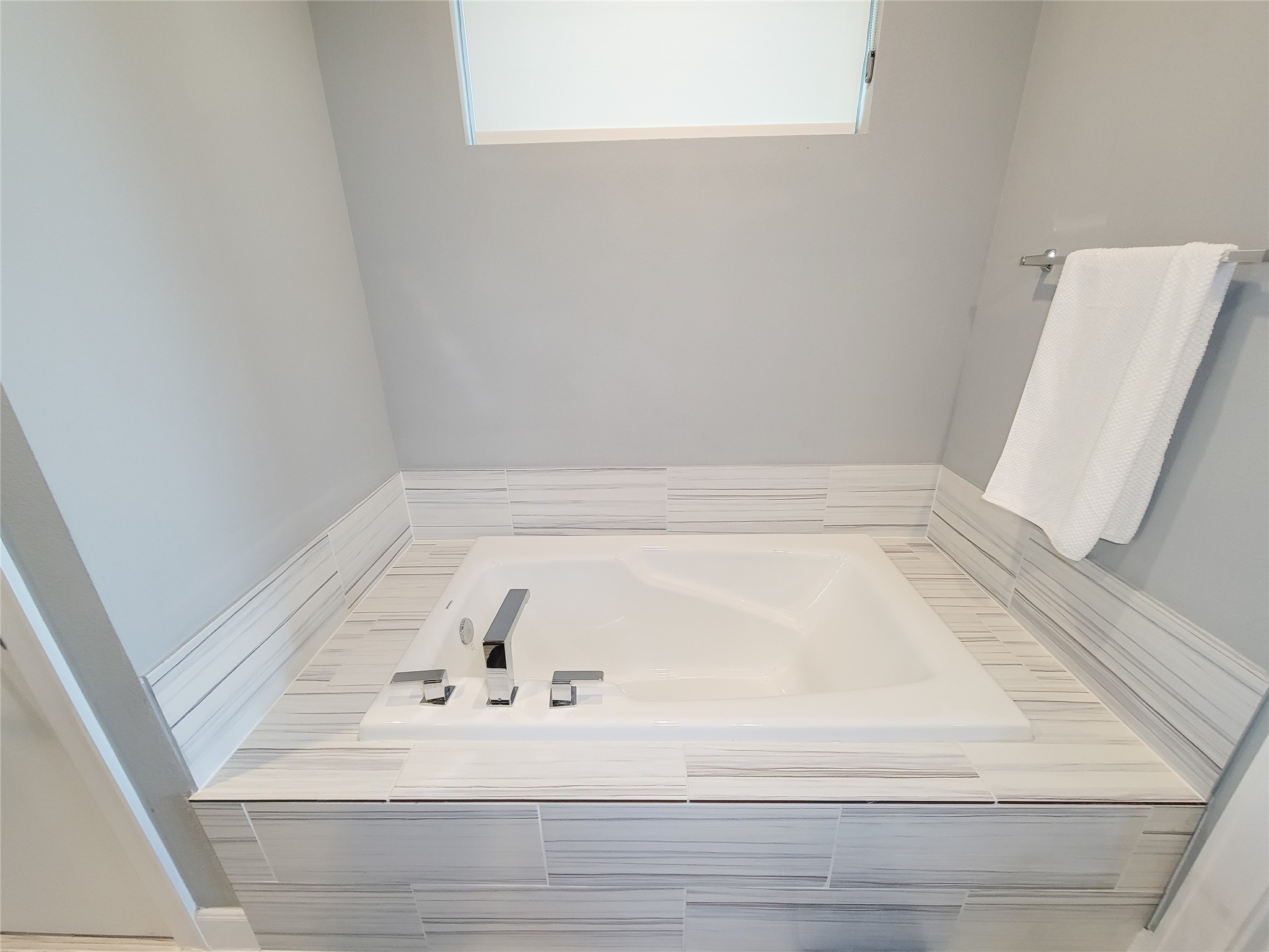 1705 Eado Point Lane Houston, TX 77003 - Photo 43 of 50 The luxurious bathroom features a sleek, modern soaking tub with a stylish tile surround. A window provides natural light, and a towel rack is conveniently placed nearby, offering a clean and inviting space for relaxation.