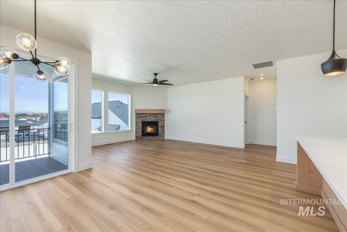 775 Pinehurst Street Payette, ID 83661 - Photo 10 of 36 Unfurnished living room featuring a textured ceiling, light wood-type flooring, a fireplace, a chandelier, and a ceiling fan