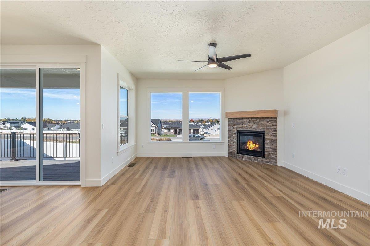 775 Pinehurst Street Payette, ID 83661 - Photo 11 of 36 Unfurnished living room with a textured ceiling, light wood finished floors, a fireplace, a ceiling fan, and a residential view