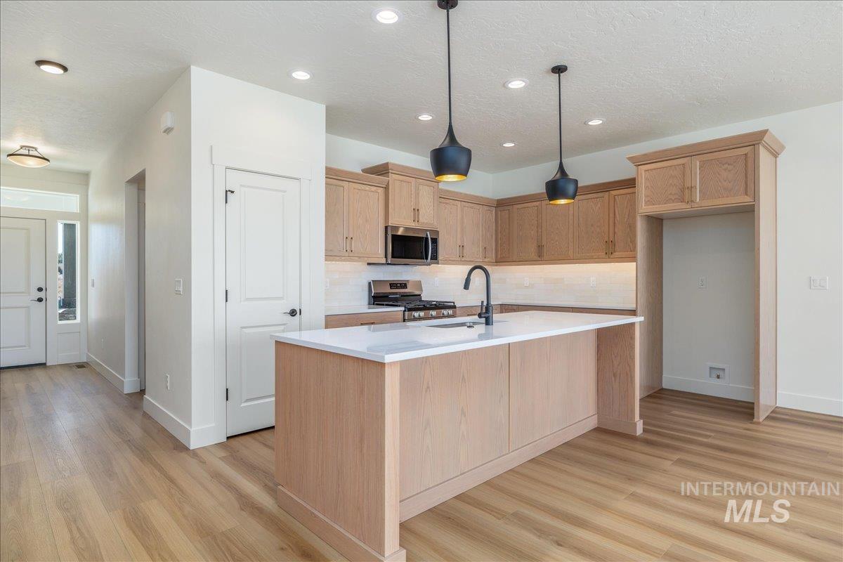 775 Pinehurst Street Payette, ID 83661 - Photo 5 of 36 Kitchen with a textured ceiling, light brown cabinets, decorative backsplash, stainless steel appliances, and hanging light fixtures