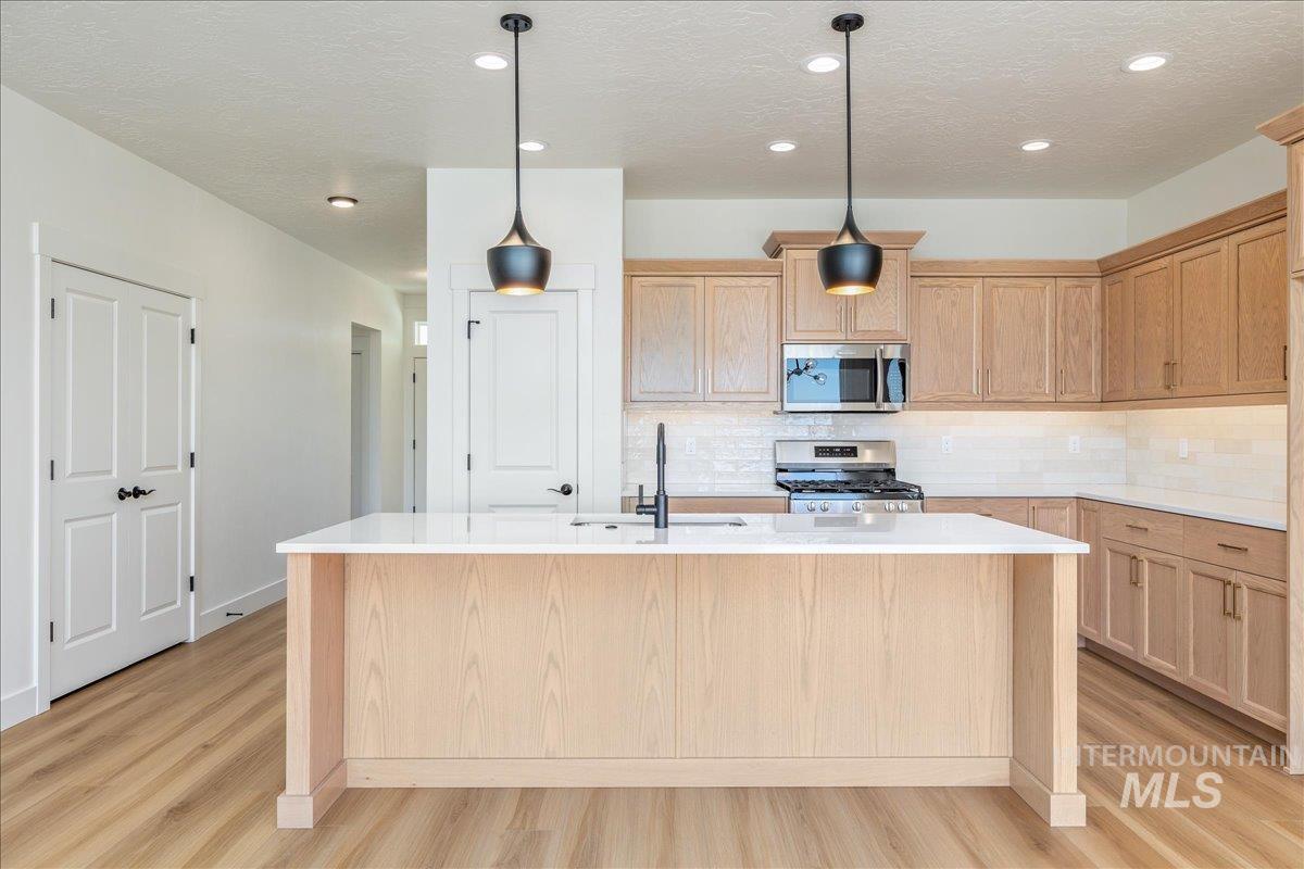 775 Pinehurst Street Payette, ID 83661 - Photo 6 of 36 Kitchen with light brown cabinetry, decorative backsplash, appliances with stainless steel finishes, a textured ceiling, and light stone countertops