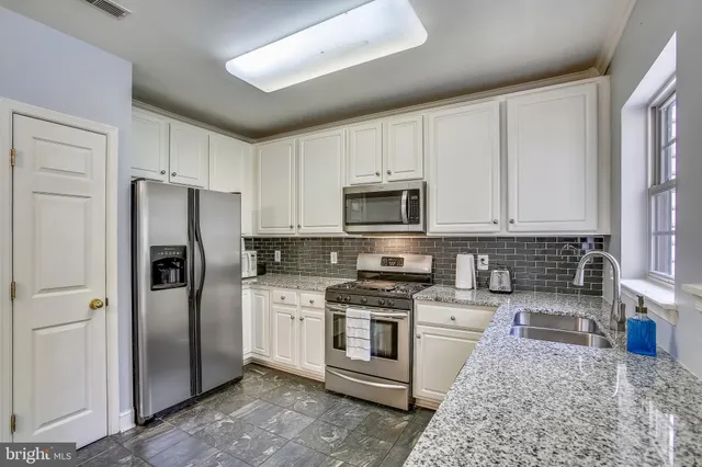 a kitchen with stainless steel appliances granite countertop a refrigerator a stove a sink and white cabinets