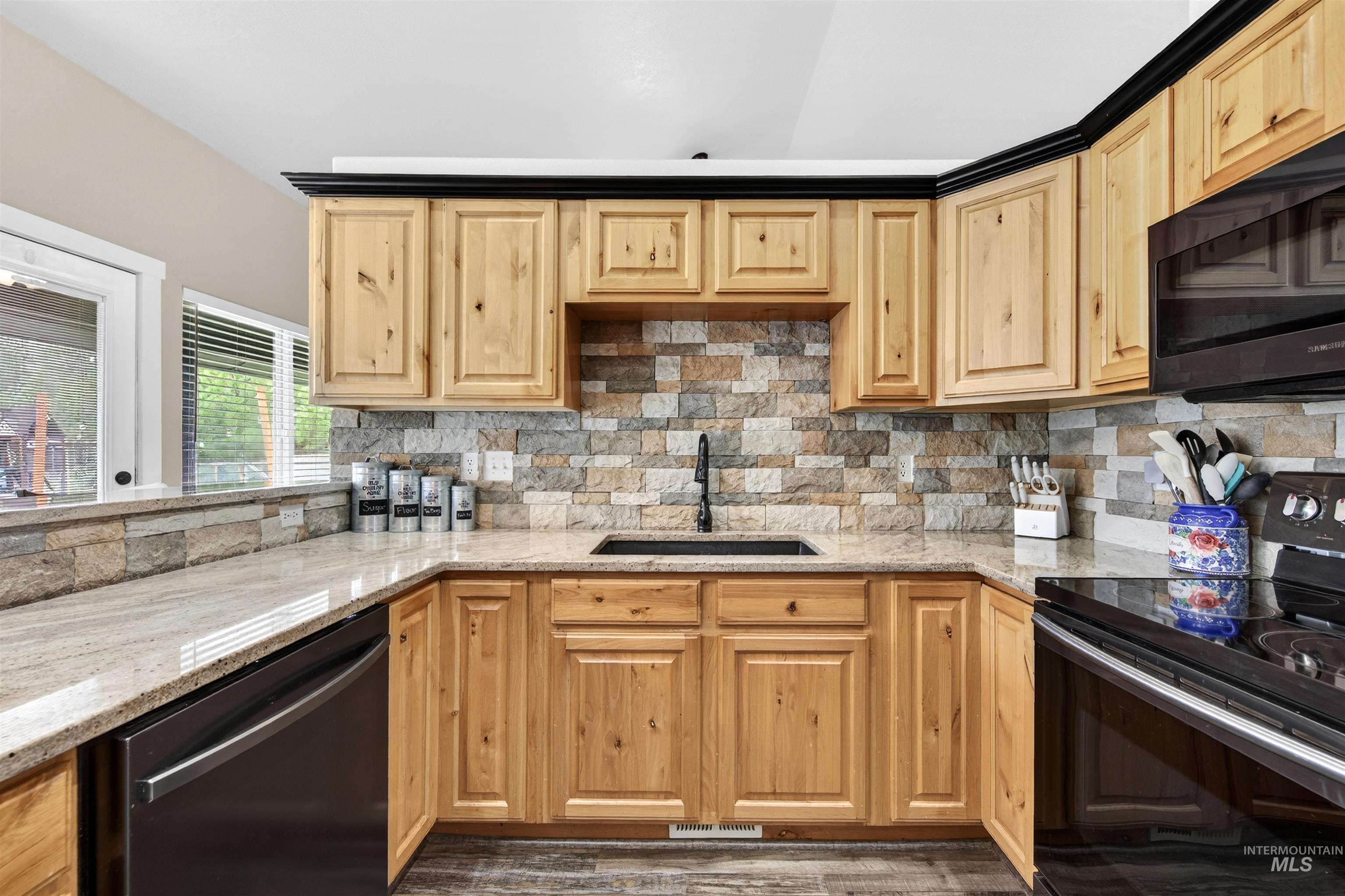 4 Round Up Circle Boise, ID 83716 - Photo 7 of 47 Kitchen featuring light wood cabinetry with black trim, granite countertops, stone tile backsplash, a black undermount sink with a matte black faucet, and black appliances