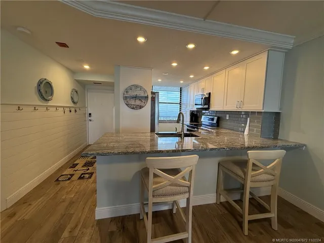 a kitchen with stainless steel appliances granite countertop a stove top oven a sink a dining table and chairs with wooden floor