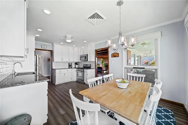 a kitchen with stainless steel appliances kitchen island granite countertop a sink a stove a refrigerator a dining table and chairs with wooden floor