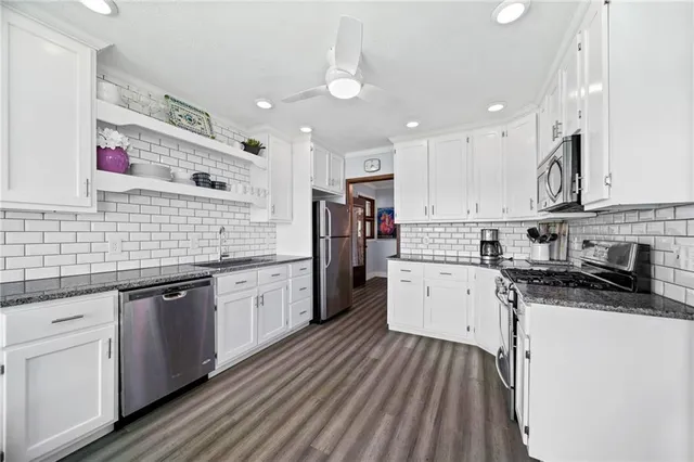 a kitchen with granite countertop white cabinets a sink dishwasher and a stove with wooden floor