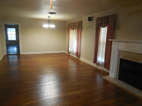 an empty room with wooden floor fireplace and windows