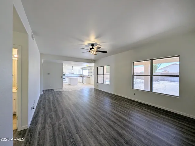 an empty room with wooden floor chandelier fan and windows