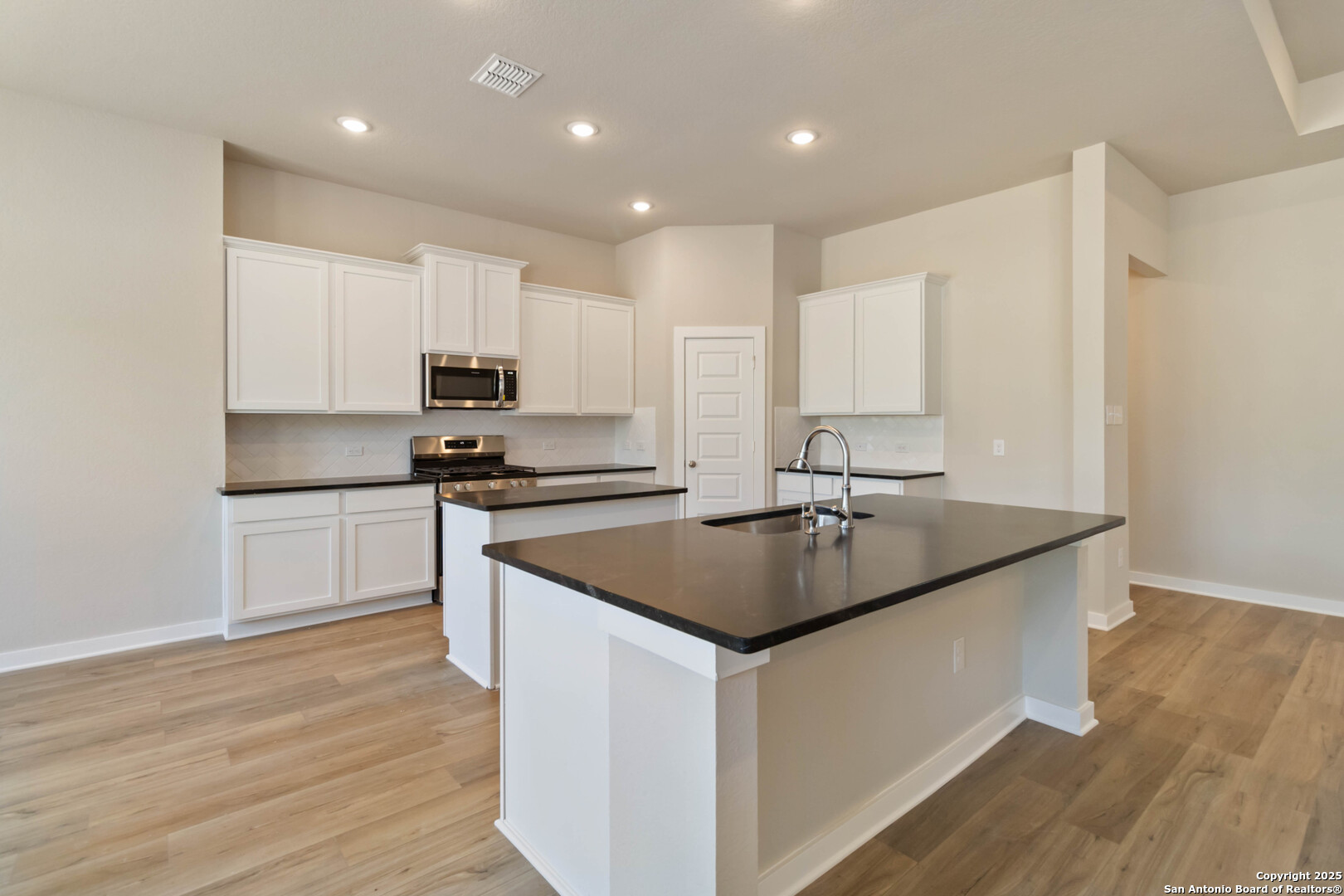 21225 Jordans Ranch Way San Antonio, TX 78264 - Photo 8 of 30 a kitchen with kitchen island granite countertop a sink and a stove top oven with wooden floors