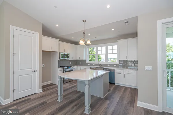 a kitchen with stainless steel appliances granite countertop a refrigerator a sink dishwasher a stove and white countertops with wooden floor