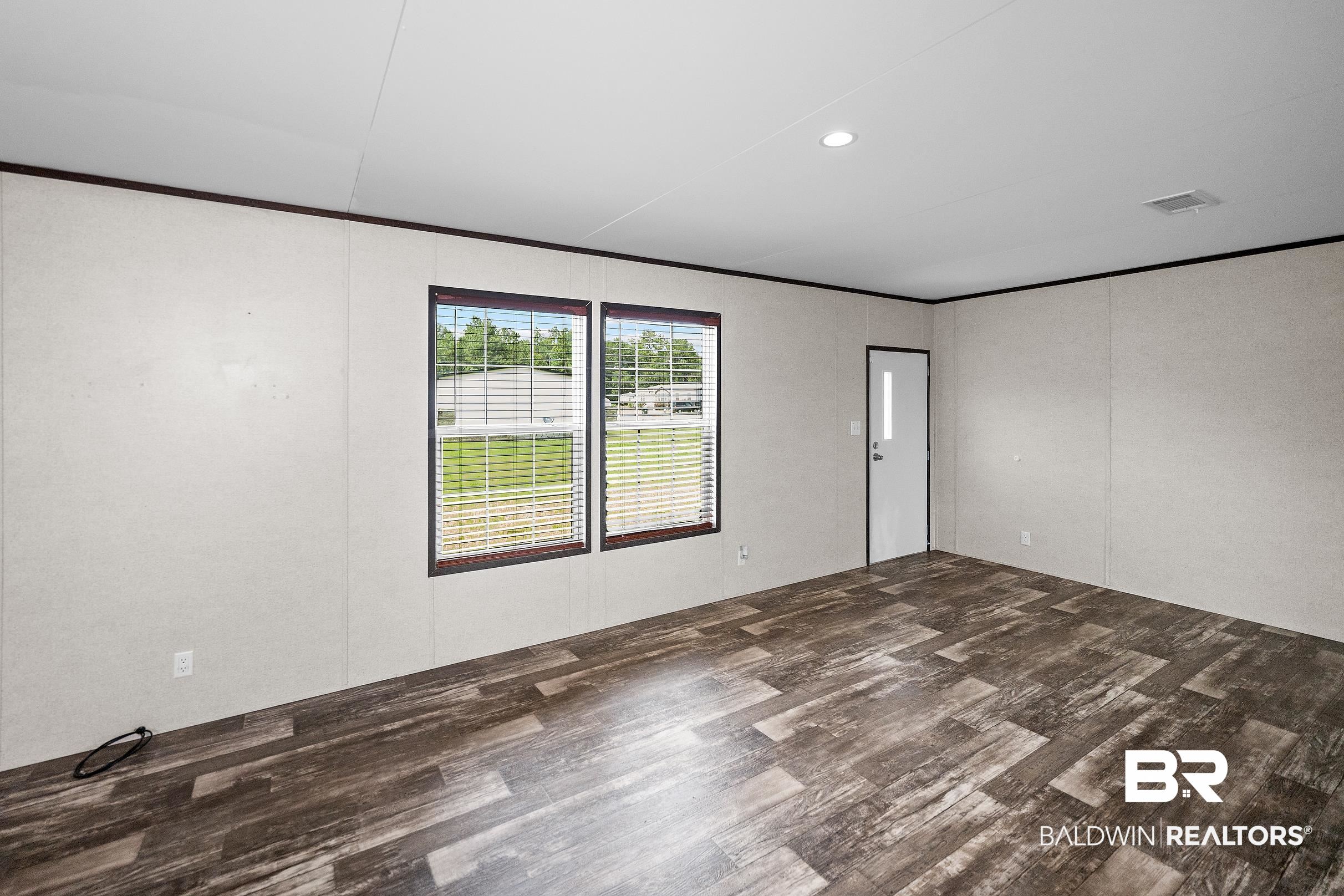 21601 Westside Loop Silverhill, AL 36576 - Photo 11 of 42 Spacious room featuring wood-finish flooring, two large windows with blinds, a white entry door with a vertical window, recessed lighting, and light-toned walls with dark trim