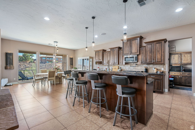 2376 Stone Crest Circle St. George, UT 84790 - Photo 10 of 61 Kitchen with hanging light fixtures, a kitchen bar, dark stone counters, and a kitchen island with sink